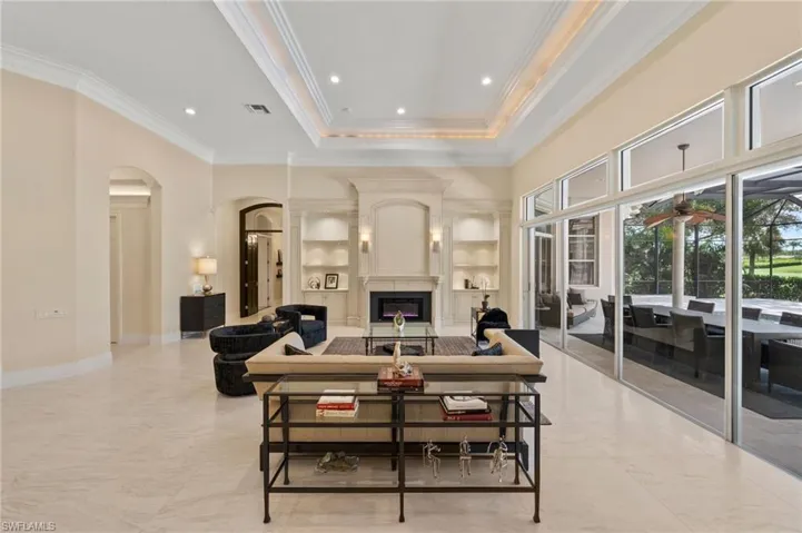 Living room with arched walkways, built in shelves, a large fireplace, ornamental molding, and recessed lighting