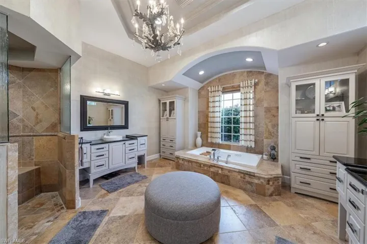 Full bathroom featuring vanity, a bath, walk in shower, tile walls, and stone tile floors