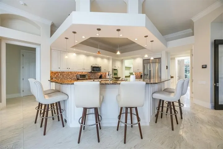 Kitchen with tasteful backsplash, a tray ceiling, decorative light fixtures, ornamental molding, and a peninsula