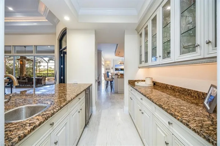 Bar with a raised ceiling, ornamental molding, dark stone counters, white cabinetry, and glass insert cabinets