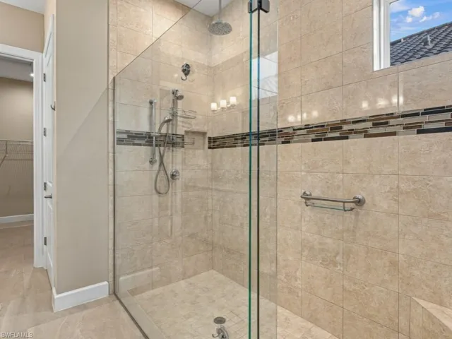Walk-in shower featuring floor-to-ceiling stone-finish tile, decorative glass mosaic accent inlay, frameless glass enclosure, built-in tiled bench, and rain shower head