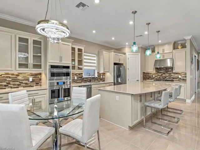 Kitchen featuring off-white cabinetry, stone-tiled backsplash, oversized central island with stone countertop, stainless steel double wall ovens, and neutral tile flooring