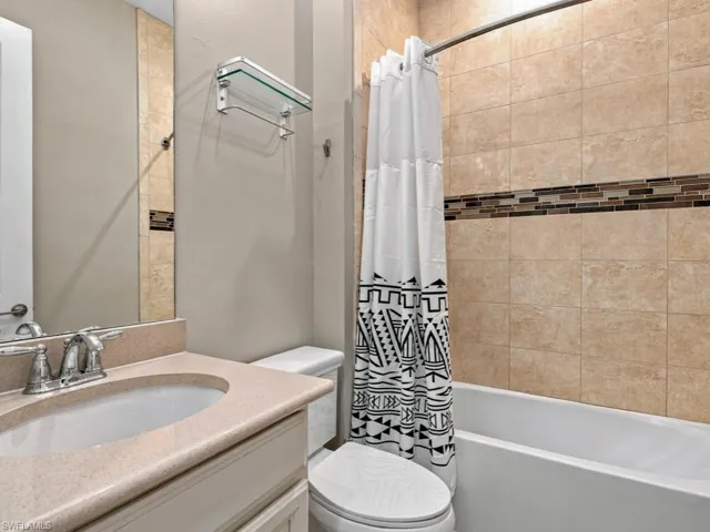 Bathroom featuring a vanity with a solid-surface countertop, an integrated sink, a glass-shelf wall fixture, and a tub-shower combination with tiled walls and a decorative mosaic border