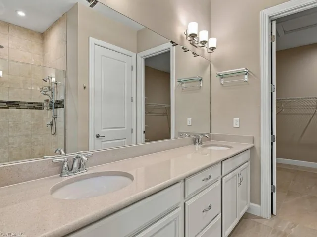 Dual-vanity bathroom featuring a solid-surface countertop with integrated sinks, white cabinetry, a floor-to-ceiling mirror, and a walk-in shower with tile surround