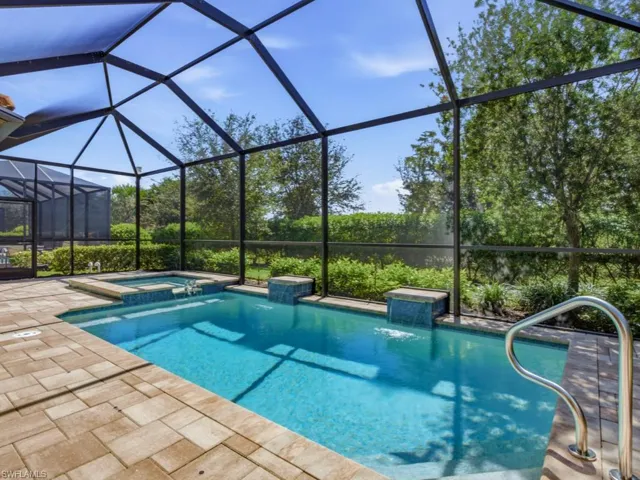 Screen-enclosed pool area featuring a spillover spa, tiled water features, paver decking, and a metal handrail