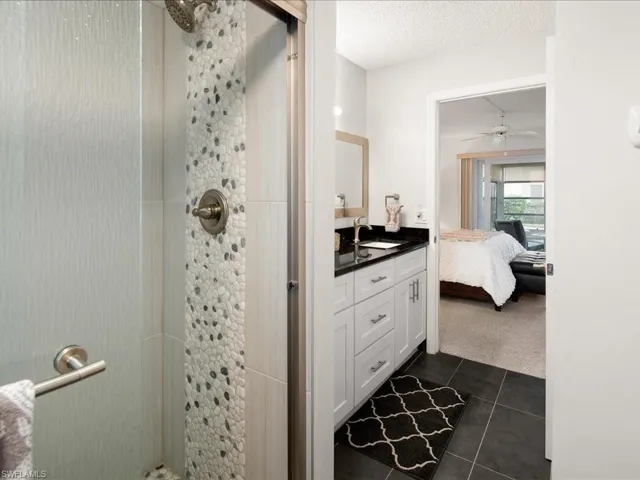 Ensuite bathroom with vanity, tile patterned floors, a ceiling fan, connected bathroom, and a tile shower