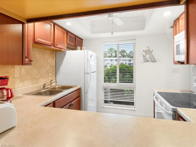Kitchen with tasteful backsplash, white appliances, a ceiling fan, a raised ceiling, and a sink