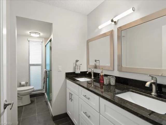 Remodeled full master bathroom featuring toilet, a double sink, a shower stall, and tile patterned flooring