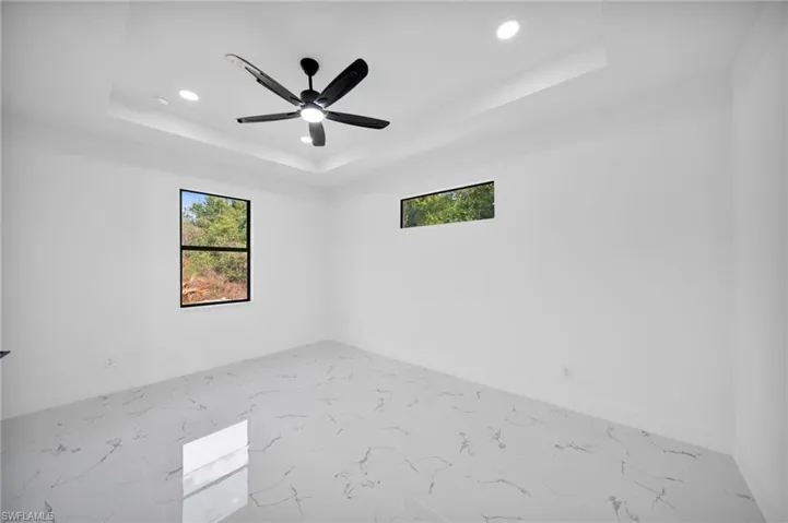 Spare room featuring recessed lighting, plenty of natural light, a ceiling fan, a raised ceiling, and marble look tiles