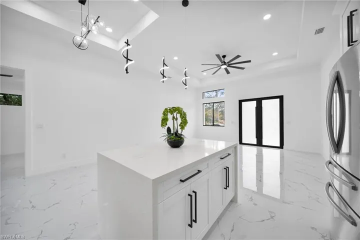 Kitchen featuring white cabinetry, a raised ceiling, freestanding refrigerator, open floor plan, and light stone countertops