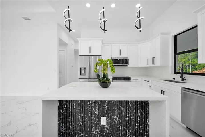 Kitchen featuring light stone countertops, stainless steel appliances, white cabinetry, a kitchen island, and recessed lighting