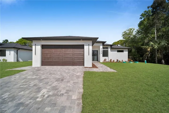 Prairie-style home with a front lawn, decorative driveway, and stucco siding