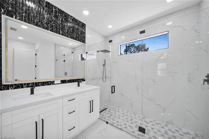 Full bathroom with double vanity, a marble finish shower, recessed lighting, stone wall, and light marble finish flooring