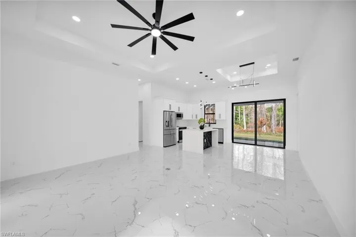 Unfurnished living room with a raised ceiling, ceiling fan, light marble finish flooring, and suspended lighting