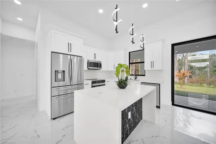 Kitchen featuring a center island, stainless steel appliances, white cabinetry, light stone counters, and recessed lighting