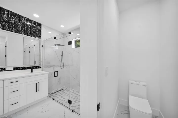Bathroom featuring recessed lighting, light marble finish floors, a marble finish shower, and vanity