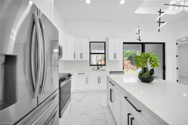 Kitchen with stainless steel appliances, white cabinetry, light stone countertops, and light marble finish flooring