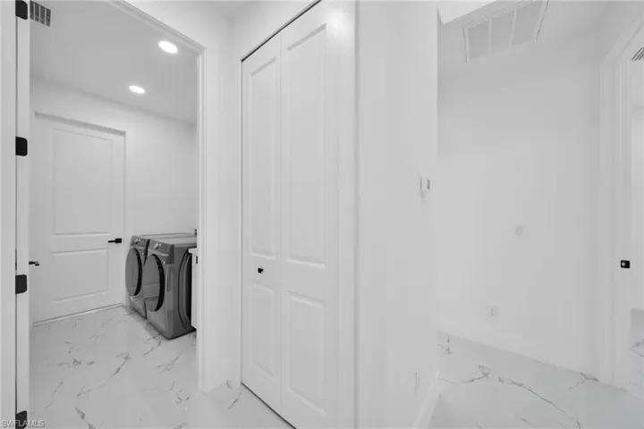 Laundry area featuring recessed lighting, light marble finish floors, and washer and clothes dryer