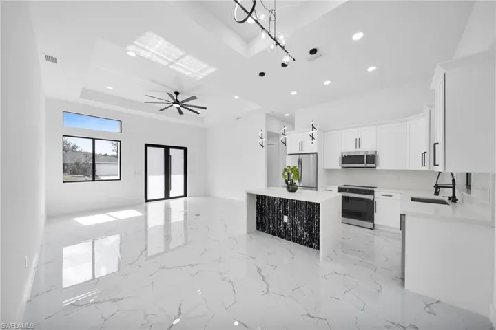 Kitchen with open floor plan, stainless steel appliances, light marble finish floors, light stone countertops, and white cabinets