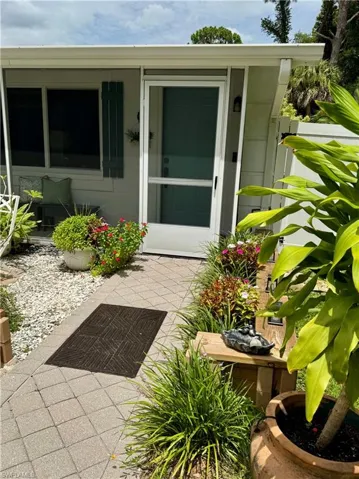 Entryway featuring a screen door, decorative teal shutters, a paver walkway, and lush landscaping