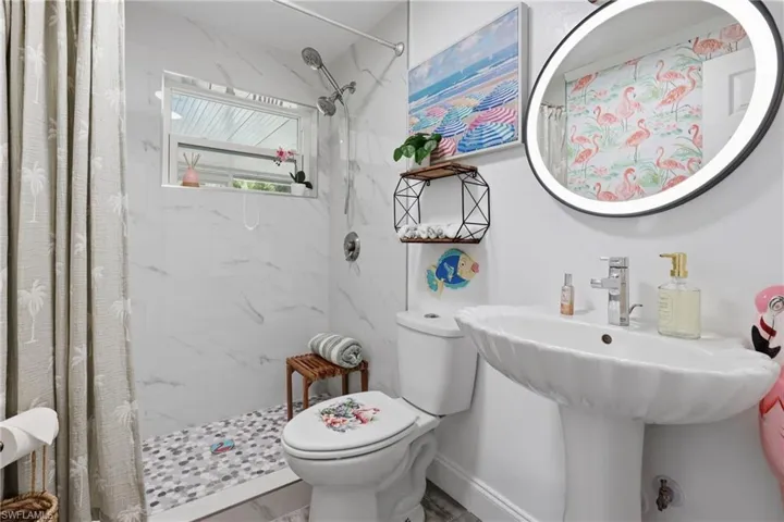 Contemporary bathroom featuring a pedestal sink, a wall-mounted illuminated mirror, and a shower with white tile surround and mosaic tile flooring