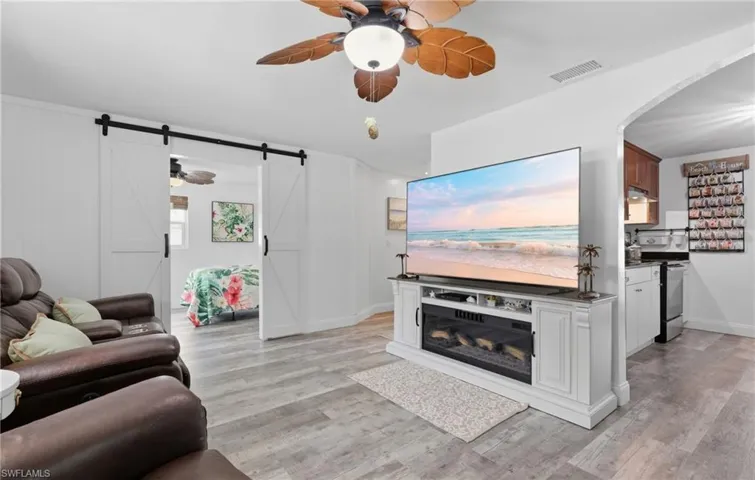 Living area featuring light flooring, white walls, and a ceiling fan with leaf-shaped blades