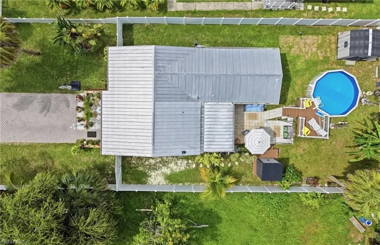 Expansive property featuring a metal roof, a paved driveway, a fenced yard, a patio area, and an above-ground pool with an accompanying deck