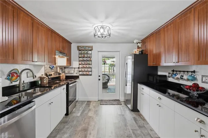 Contemporary kitchen featuring wood-finish upper cabinetry, white lower cabinetry, black countertops, and stainless steel appliances