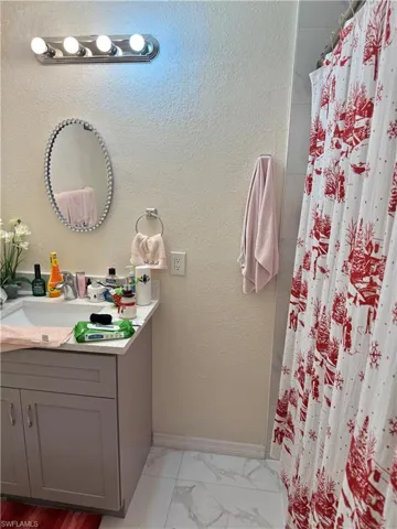 Full bath featuring vanity, curtained shower, a textured wall, and light marble finish floors