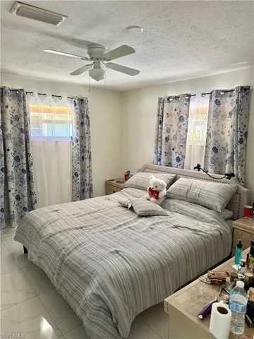 Tiled bedroom featuring multiple windows, a ceiling fan, and a textured ceiling