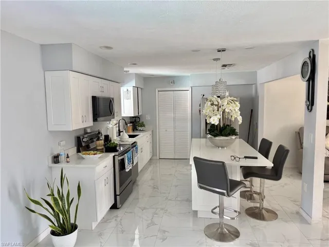 Kitchen featuring stainless steel appliances, a breakfast bar area, a kitchen island, light marble finish flooring, and white cabinetry