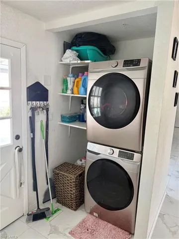Laundry area featuring stacked washer and clothes dryer, light marble finish floors, and a textured ceiling