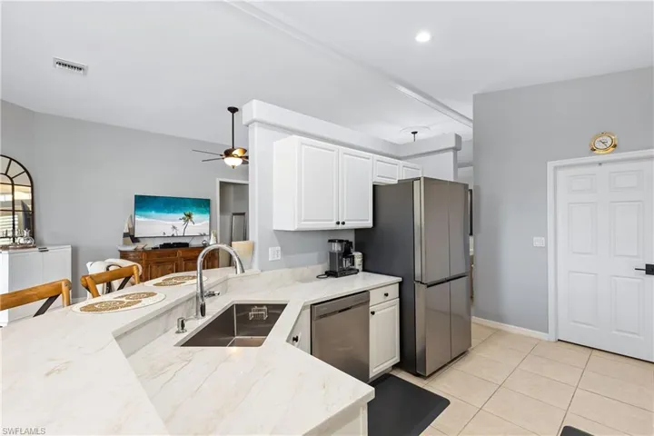 Kitchen with white cabinets, sink, ceiling fan, light stone countertops, and stainless steel appliances