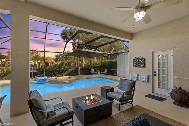 Pool at dusk with ceiling fan, an outdoor fire pit, a lanai, a patio area, and an in ground hot tub