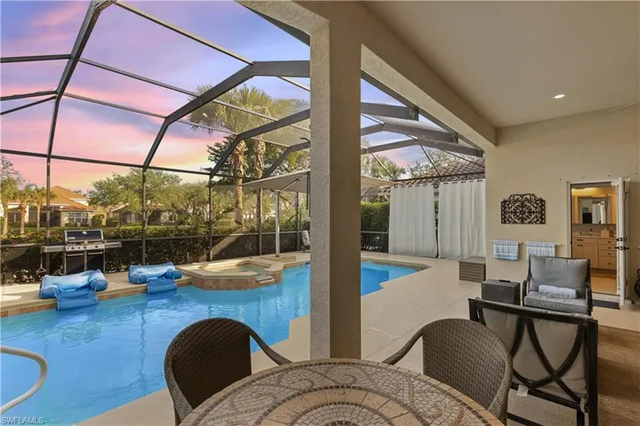 Pool at dusk with an in ground hot tub, a patio, and glass enclosure