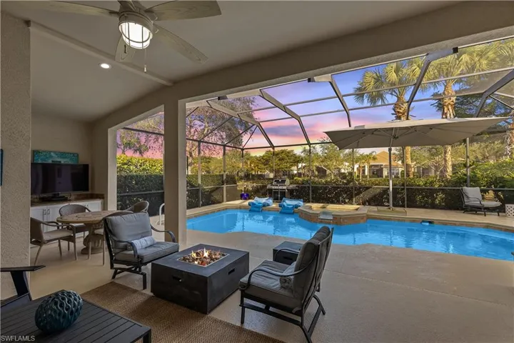 Pool at dusk featuring ceiling fan, an outdoor fire pit, a lanai, a patio area, and an in ground hot tub