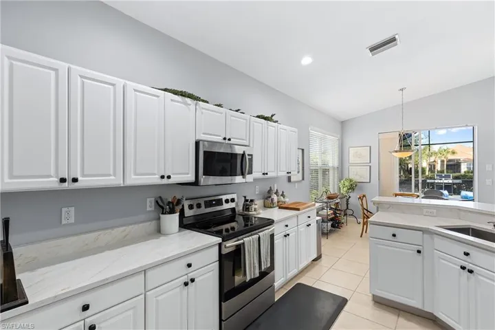 Kitchen with white cabinetry, sink, stainless steel appliances, pendant lighting, and vaulted ceiling