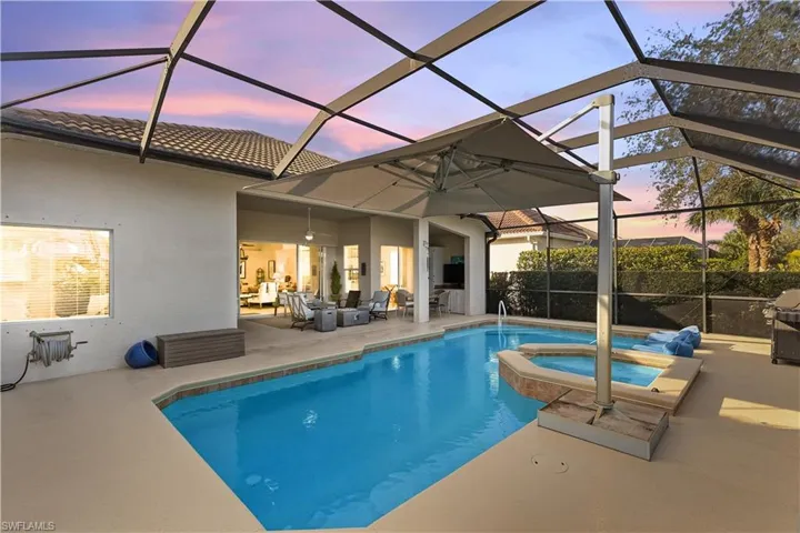 Pool at dusk with glass enclosure, an in ground hot tub, and a patio