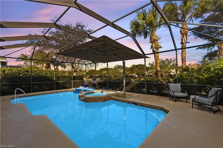 Pool at dusk featuring glass enclosure, an in ground hot tub, and a patio area