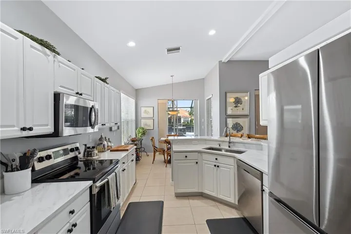 Kitchen with stainless steel appliances, white cabinetry, lofted ceiling, and sink