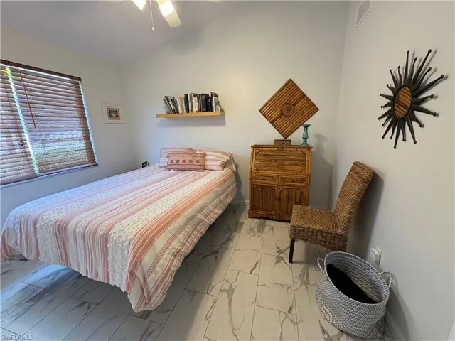 Bedroom with lofted ceiling, light marble finish floors, and ceiling fan