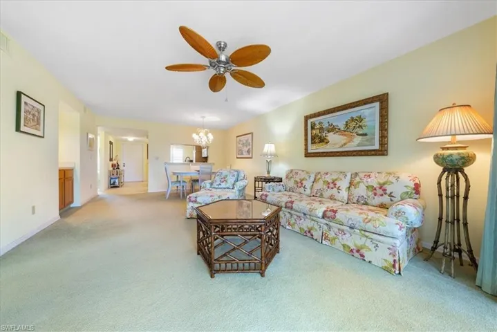 Living room featuring ceiling fan with notable chandelier, baseboards, and light carpet