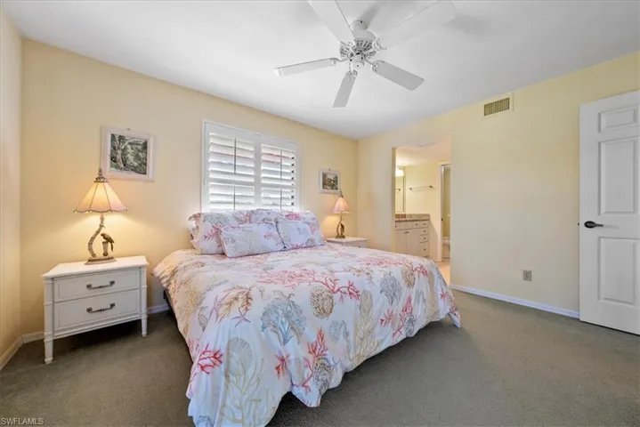 Carpeted bedroom featuring visible vents, baseboards, ceiling fan, and ensuite bathroom