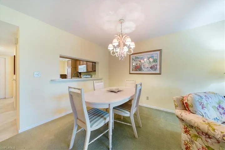 Dining space featuring light colored carpet, baseboards, and a notable chandelier