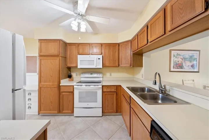 Kitchen featuring brown cabinets, a ceiling fan, a sink, white appliances, and light tile patterned floors