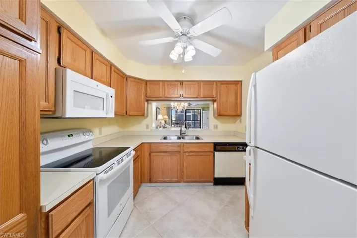 Kitchen with a ceiling fan, a sink, white appliances, light countertops, and light tile patterned floors