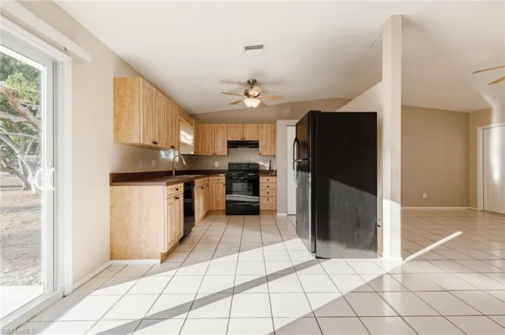 Kitchen with black appliances, sink, ceiling fan, vaulted ceiling, and light tile patterned floors