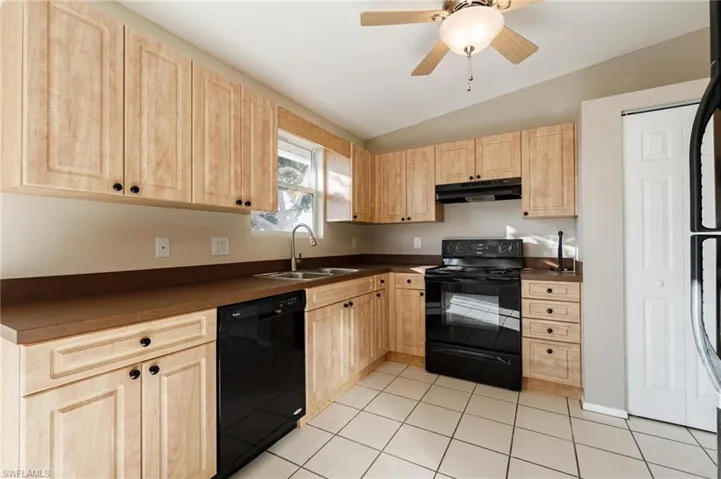 Kitchen with light brown cabinets, light tile patterned floors, vaulted ceiling, black appliances, and sink