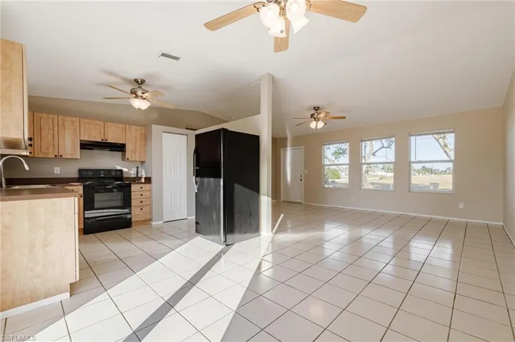 Kitchen featuring sink, black appliances, light brown cabinets, and lofted ceiling