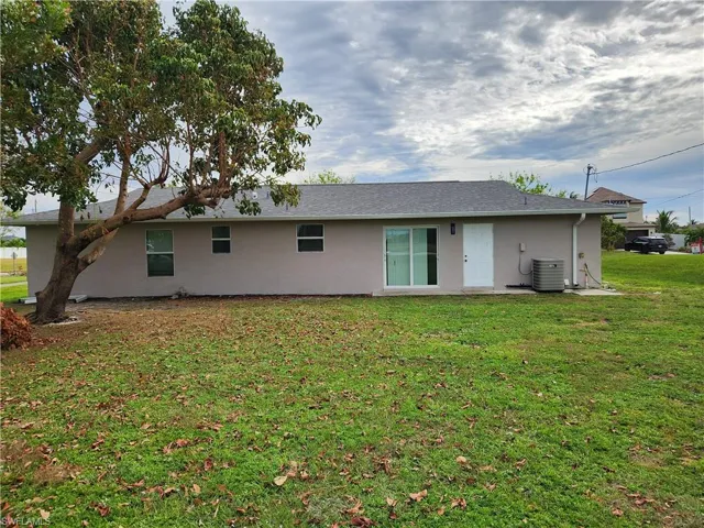 Back of property with cooling unit and a lawn